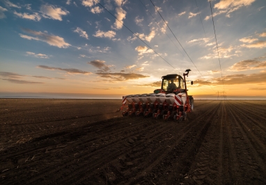 A tractor with a planter, running in a field with a nice sunset behind it.